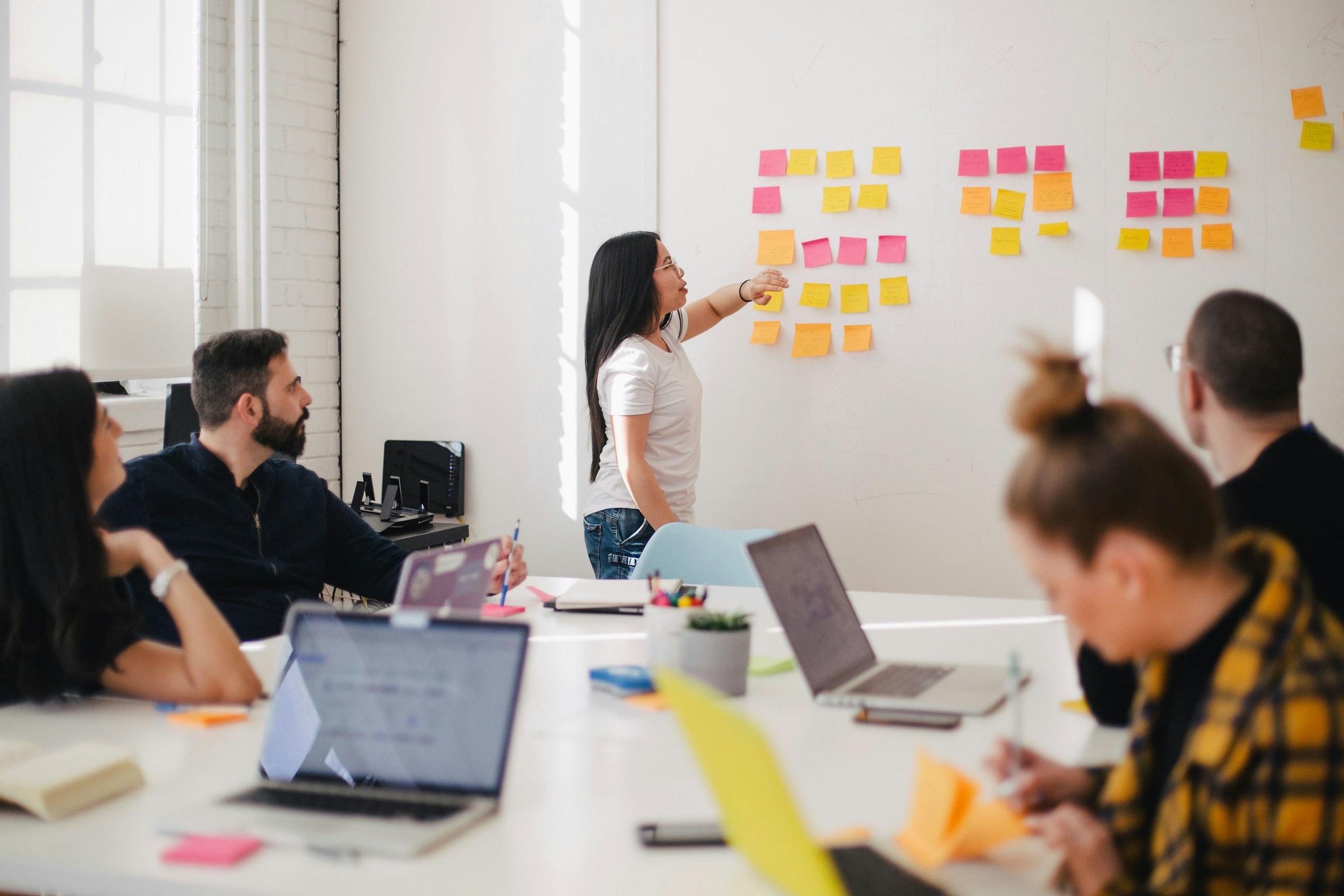 A collaborative brainstorming session in a conference room, with a person pointing at sticky notes on a whiteboard.