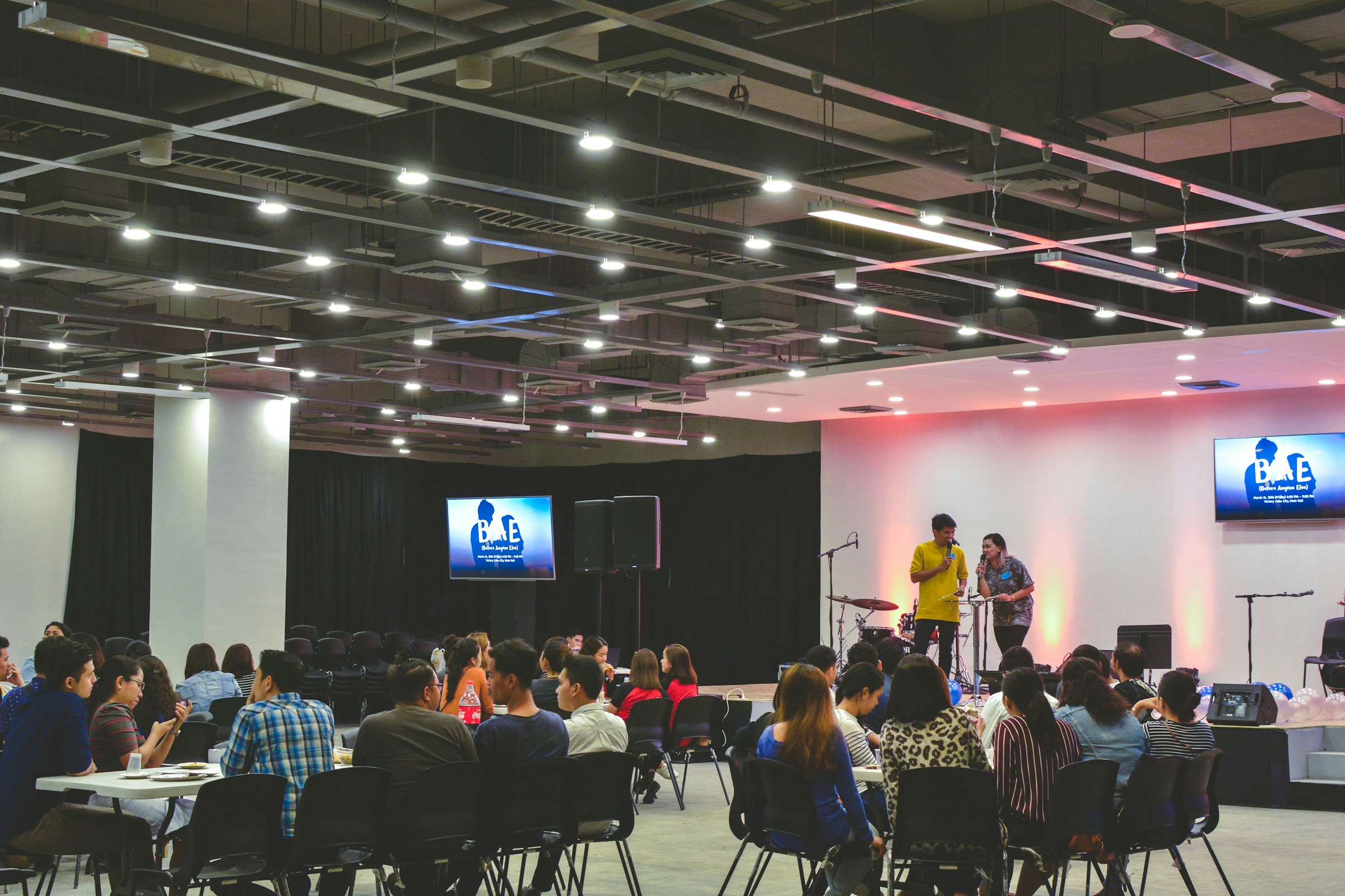 Attendees seated in a conference room listening to a speaker with a microphone.